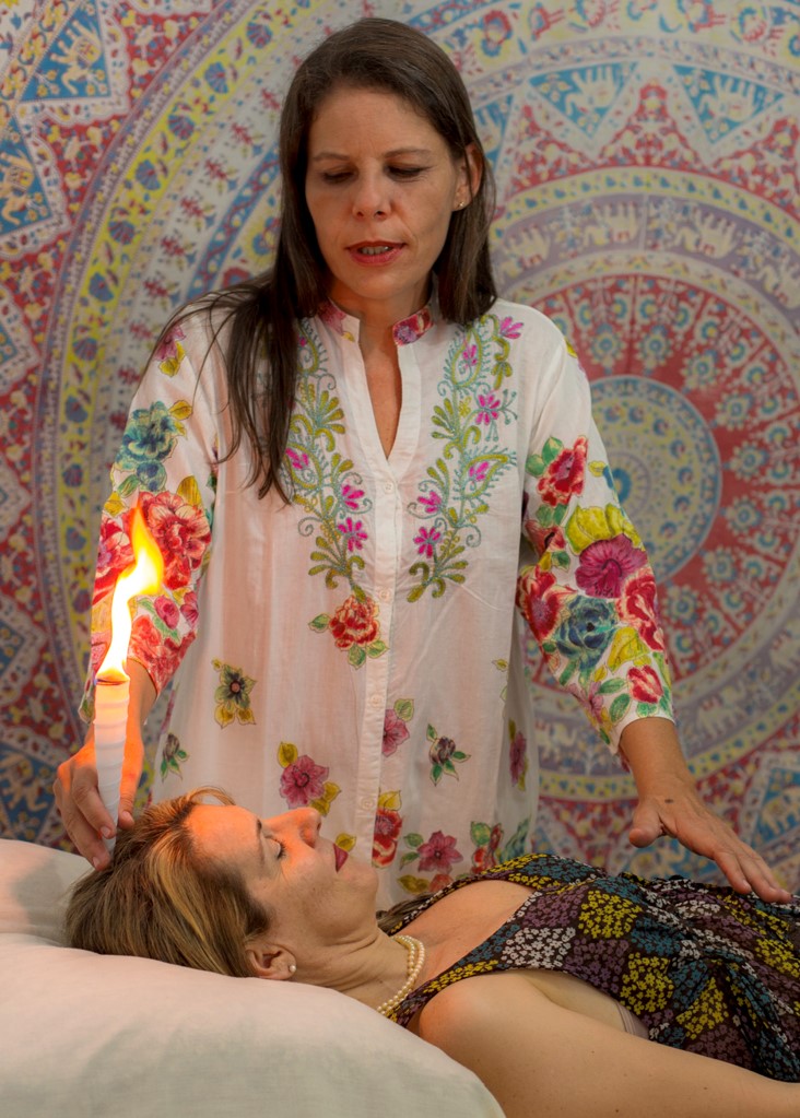 Mulher branca deitada de barriga para cima, Mulher em pé, segurando um cone com fogo. limpeza energética com o cone chinês. cones chineses, cone hindu