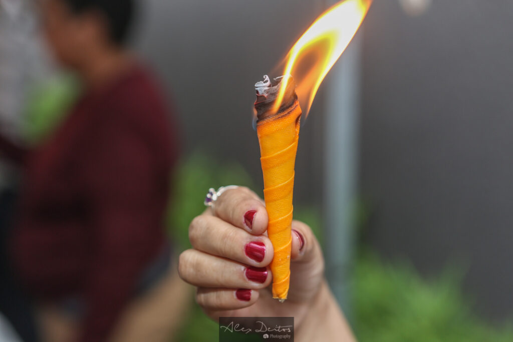 Uma mão branca segurando um cone em parafina com fogo, para realizar a Limpeza Energética